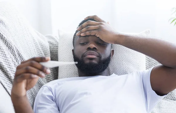 Hombre afroamericano comprobando su temperatura corporal en casa —  Fotos de Stock