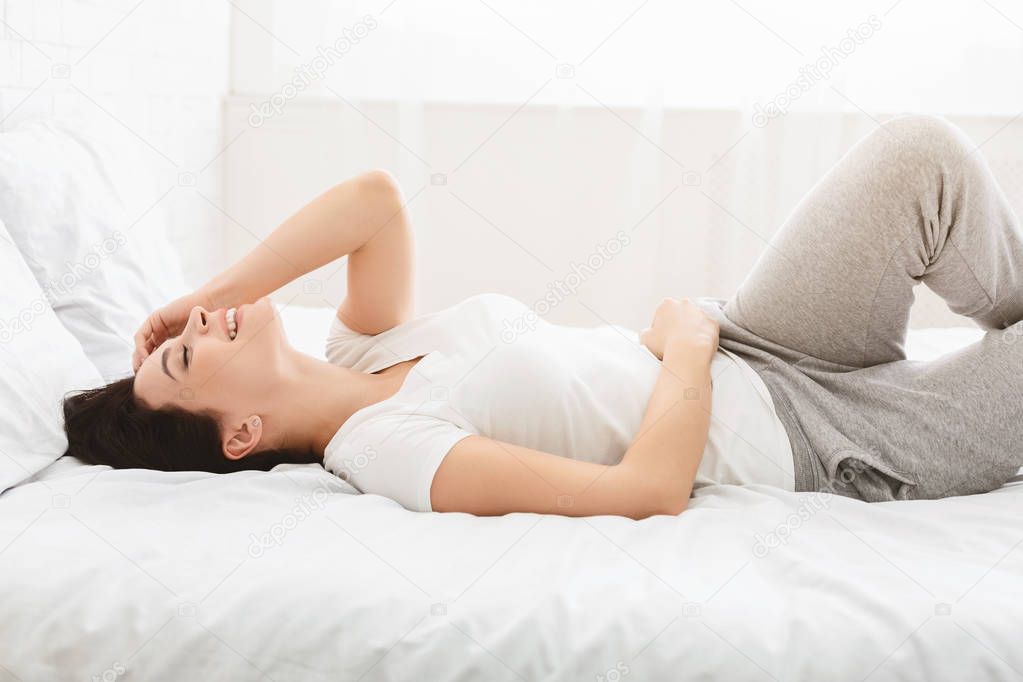 Laughing woman lying in bed early in morning