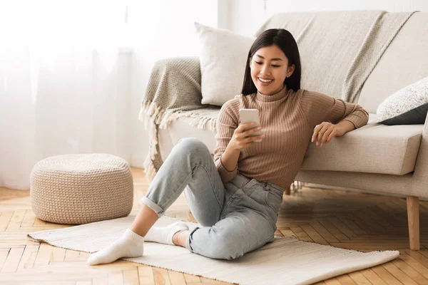 Lycklig asiatisk tjej meddelanden på telefonen hemma — Stockfoto