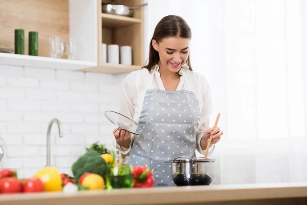 Donna agitando zuppa con cucchiaio di legno, cottura in cucina — Foto Stock