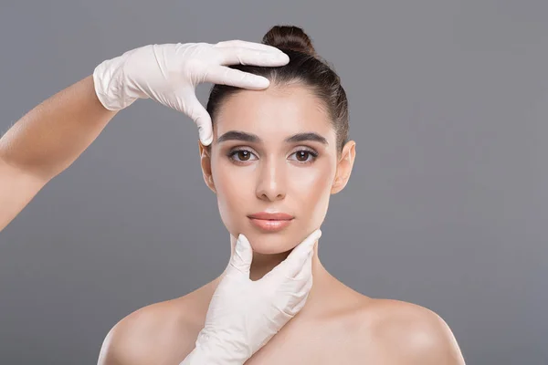 Médico en guantes toque cara de mujer, fondo gris — Foto de Stock