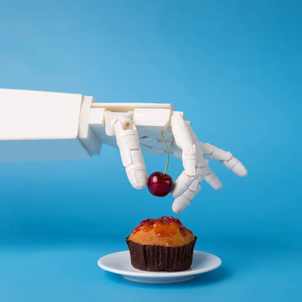 Рука робота украшает сладкий кекс свежей вишней — стоковое фото