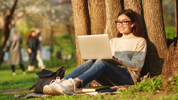 Estudiante chica surfeando red en portátil descansando cerca de árbol — Foto de Stock