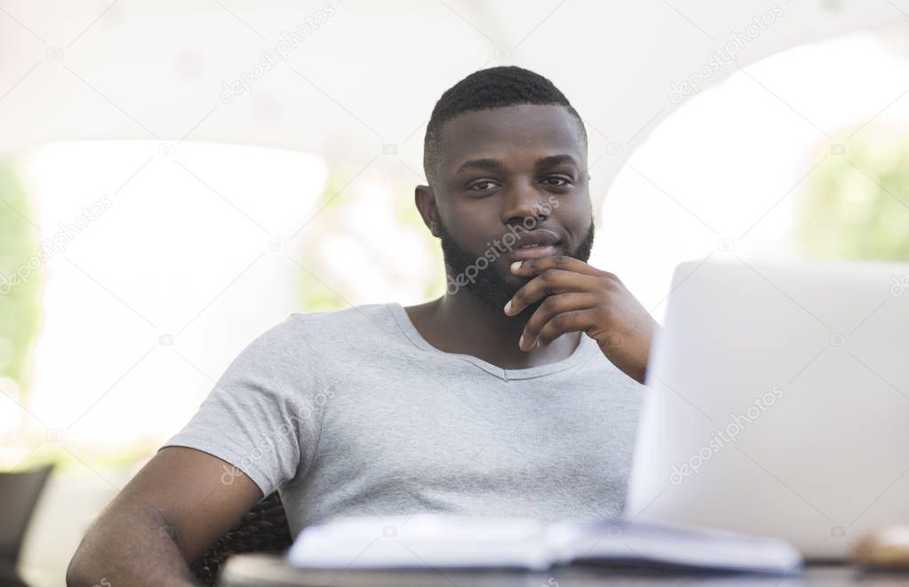 Thoughtful african american guy holding hand near chin in cafe