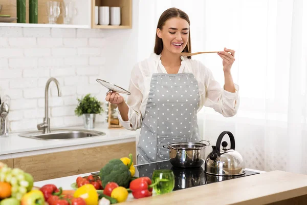 Junge Hausfrau probiert Suppe mit Kochlöffel — Stockfoto