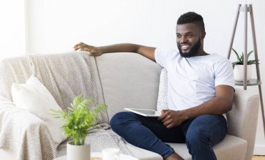 Neşeli siyah adam dijital tablet ile kanepede oturan