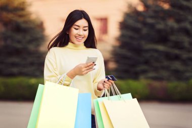 Alışveriş poşetleri ile yürüyen ve telefonda mesaj atan kız