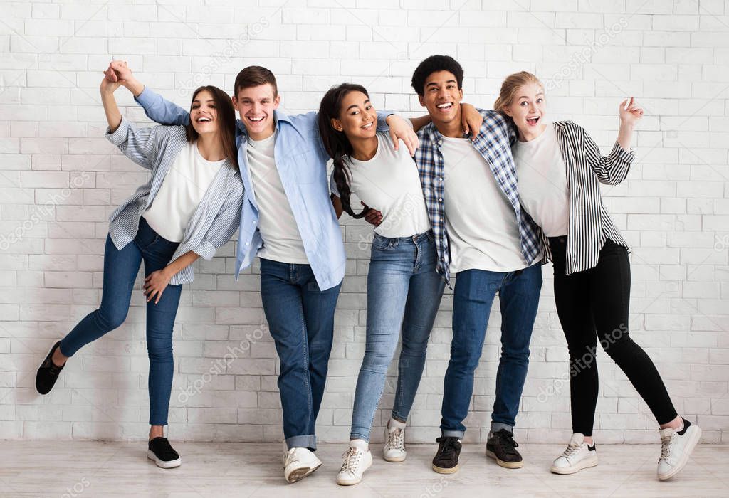 Friends embracing and having fun over white brick wall