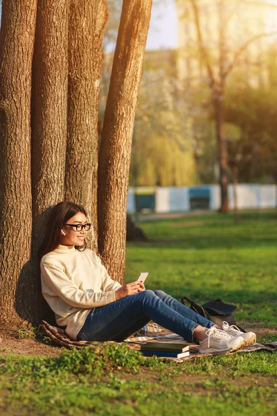 Adolescente chica charlando por teléfono, sentado bajo el árbol —  Fotos de Stock