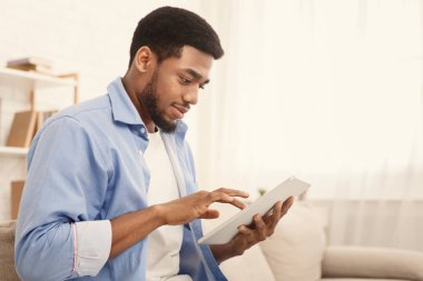 Siyah adam evde kanepede dijital tablet kullanarak