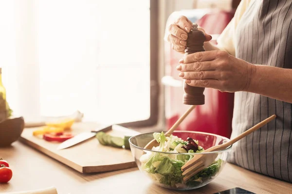 Mujer mayor condimento ensalada fresca con molino de pimienta — Foto de Stock