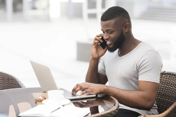 Νέος αφρικανός τύπος που εργάζεται για το laptop και μιλούν από το τηλέφωνο — Φωτογραφία Αρχείου
