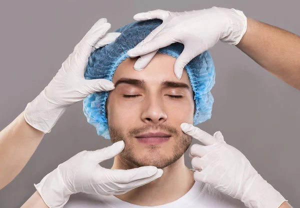 Artsen handen in handschoenen controleren gezicht van jonge man — Stockfoto