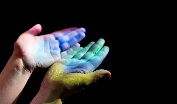 Colorful holi painted woman hands open for light on black — Stock Photo, Image