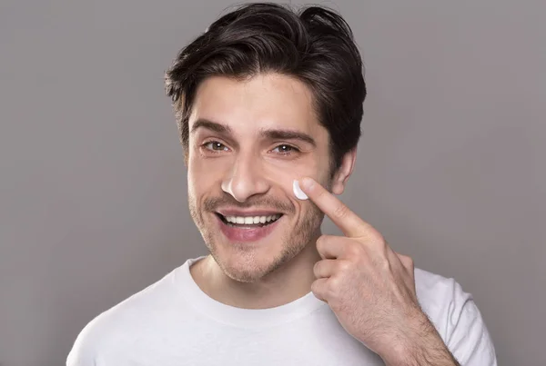 Giovane uomo che applica la crema viso sulla guancia — Foto Stock