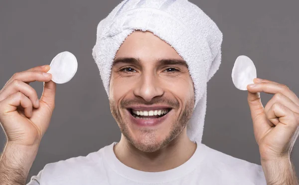 Young man with cleaning face with cotton pads with towel on his head