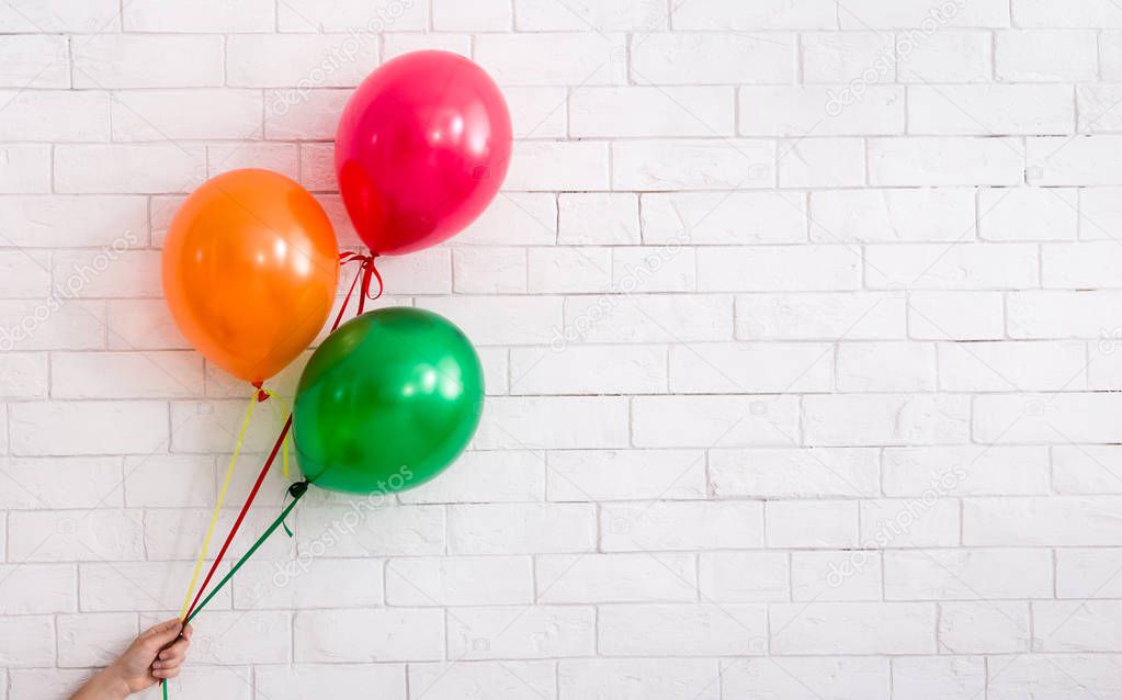Colorful party balloons in woman hand on bricks wall