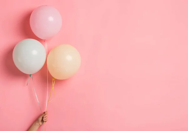 Куча шариков для вечеринок в женской руке на розовом фоне — стоковое фото