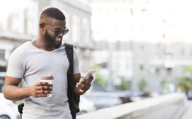 Neşeli Afrikalı adam akıllı telefon kullanarak ve kahve içme