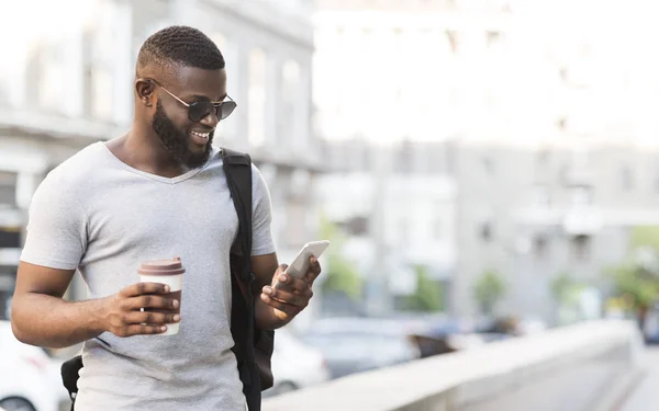 Homem africano alegre usando seu smartphone e bebendo café — Fotografia de Stock