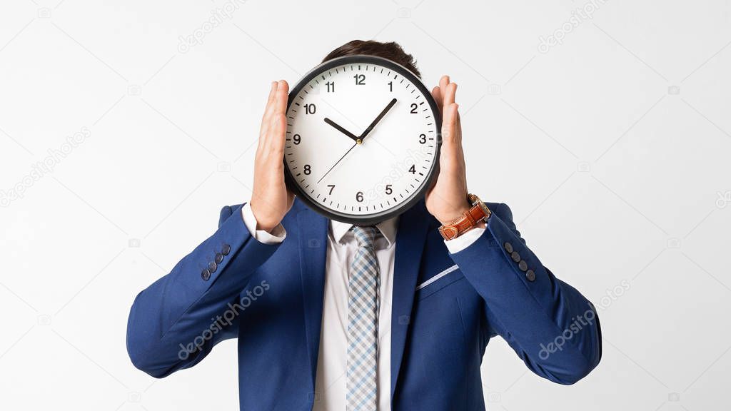 Man hiding his face behind clock on white background
