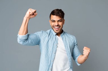 Heyecanlı adam gri stüdyo arka plan üzerinde sıkıştırılmış yumruklar sallar