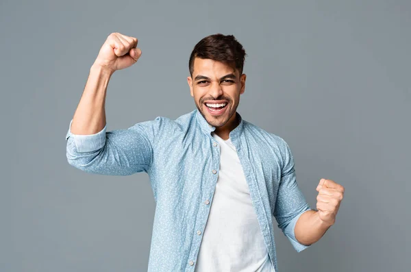 Excited guy shakes clenched fists on gray studio background