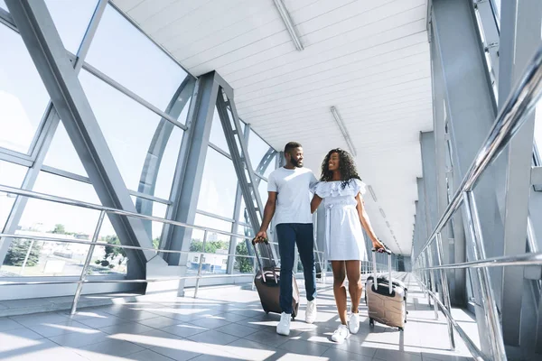 Feliz casal preto em desgaste casual indo no terminal do aeroporto com bagagem — Fotografia de Stock