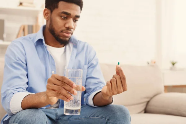 Αφρικανικός-Αμερικανός άνθρωπος κρατά ποτήρι νερό και κοιτάζοντας χάπι — Φωτογραφία Αρχείου