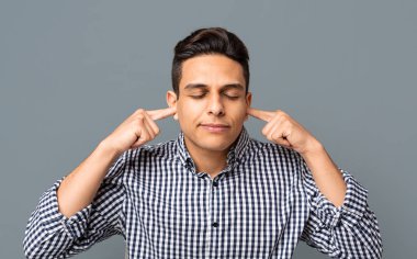 Genç adam gri arka plan üzerinde kulaklarını ve gözlerini kapatarak