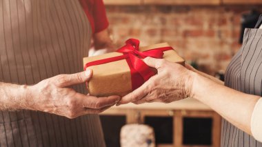 Senior man and woman sharing holiday gift at kitchen clipart