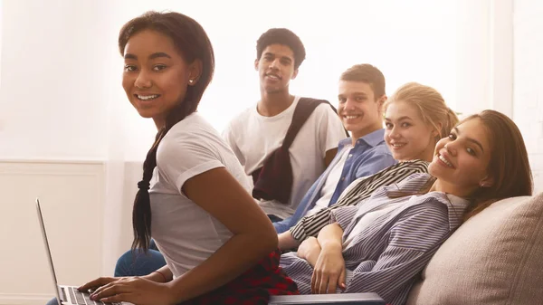 Çok ırklı genç öğrenciler kanepede kitap ve dizüstü bilgisayar ile dinleniyor — Stok fotoğraf