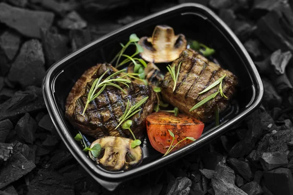 Well done beef steak with vegetables in black take away box — Stock Photo, Image