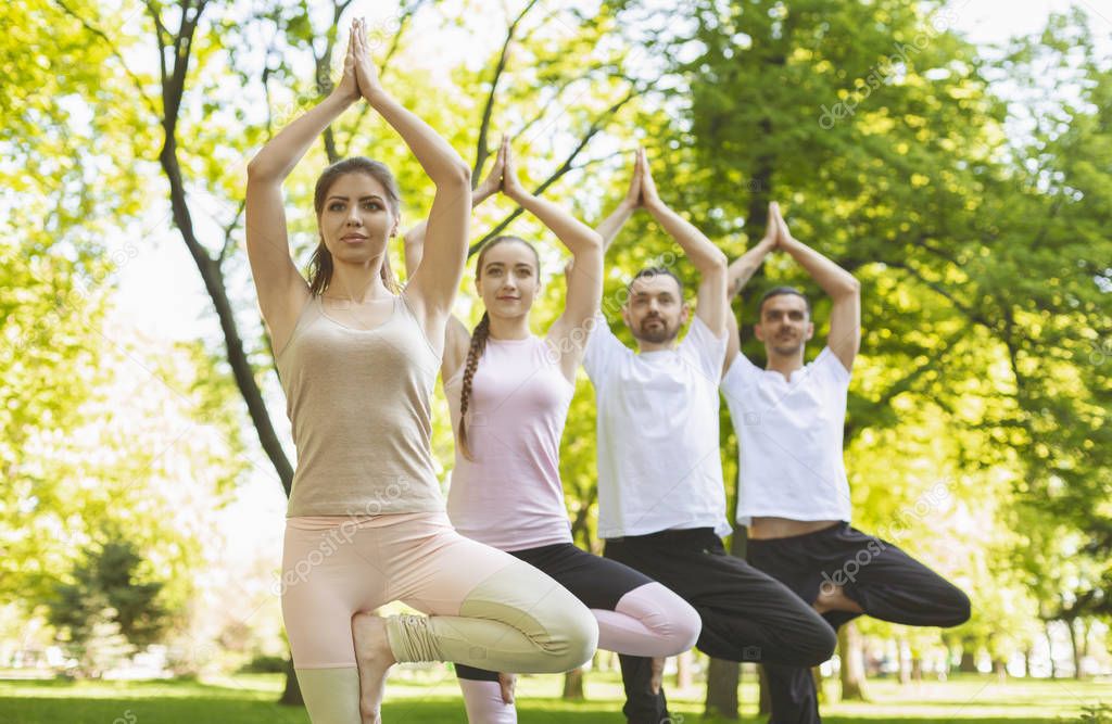 Group of yoga enthusiasts practicing Tree pose outdoors
