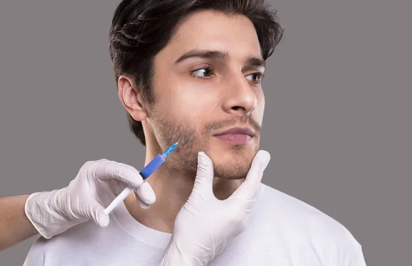 Mladý muž dostává injekci krásy, šedé pozadí ve studiu — Stock fotografie