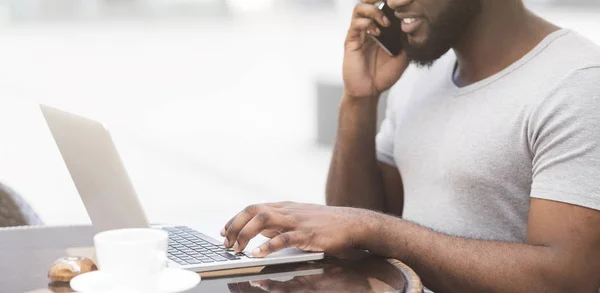 Αφρικανός Αμερικανός άντρας δακτυλογραφεί στο laptop και μιλάει στο κινητό τηλέφωνο — Φωτογραφία Αρχείου