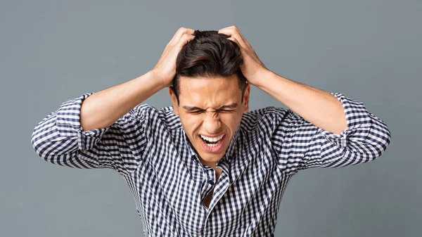 Gri arka planda saçını yolan sinirli genç adam.