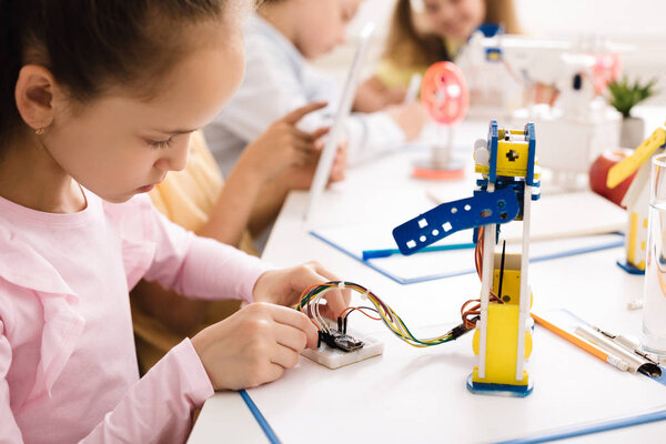 Girl building robot, working with wires in class