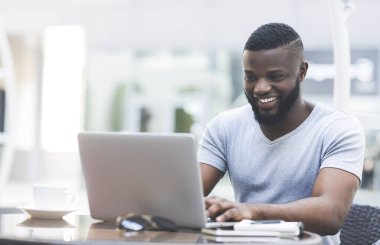 Kafede dizüstü bilgisayarda gülümseyen Afrikalı adam mesajlaşma