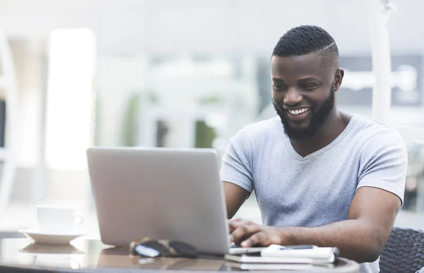 Sorrindo homem africano mensagens de texto no laptop no café — Fotografia de Stock