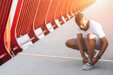 Genç afro adam güneş ışığında ayakkabı bağcıklarını kontrol
