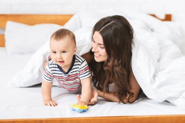 Yatakta sevimli bebek oğlu ile oynayan neşeli genç anne