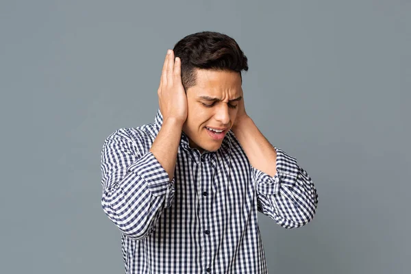 Verzweifelter Mann, der seine Ohren mit Händen vor grauem Hintergrund bedeckt — Stockfoto