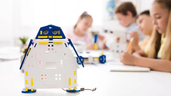 Handmade robot at desk with schoolchildren at background