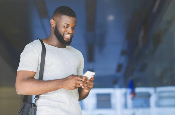 Empresário africano casual com saco enviando mensagem de texto — Fotografia de Stock