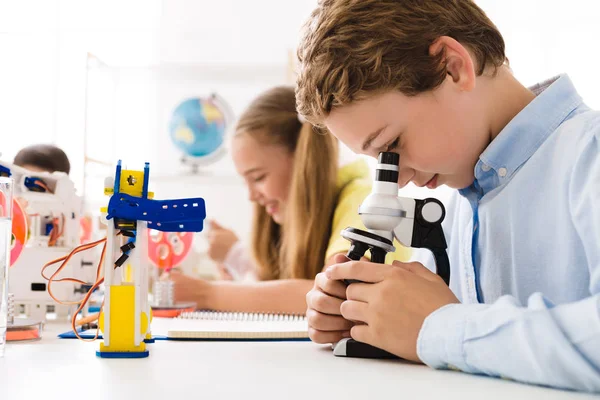 男孩看着显微镜与机器人附近 — 图库照片