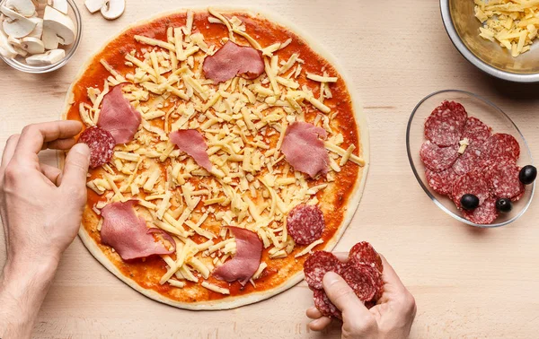 Koch legt Schinken- und Salamischeiben auf rohen Pizzaboden — Stockfoto