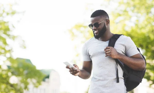 Bonito homem africano com mochila mensagens de texto no telefone — Fotografia de Stock