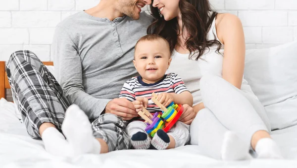 Dulce bebé sonriendo, sentado en la cama con padres cariñosos —  Fotos de Stock