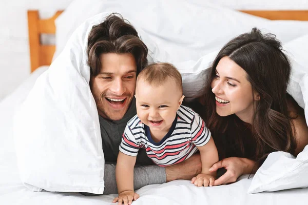 Pais alegres brincando com o bebê filho na cama — Fotografia de Stock